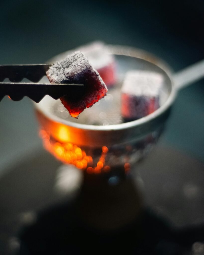 Close-up of glowing hookah charcoal with tongs in dim lighting, ideal for nightlife concepts.